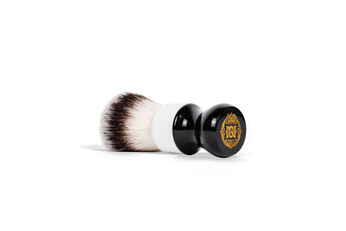 Noble Otter 26mm synthetic shave brush with black and white handle, gold logo on base, lying on its side