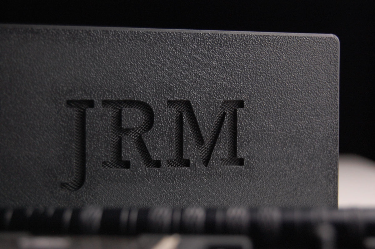 Henson razor travel case on a black background with "JRM" monogram on the lid, containing a razor and spare blades inside.