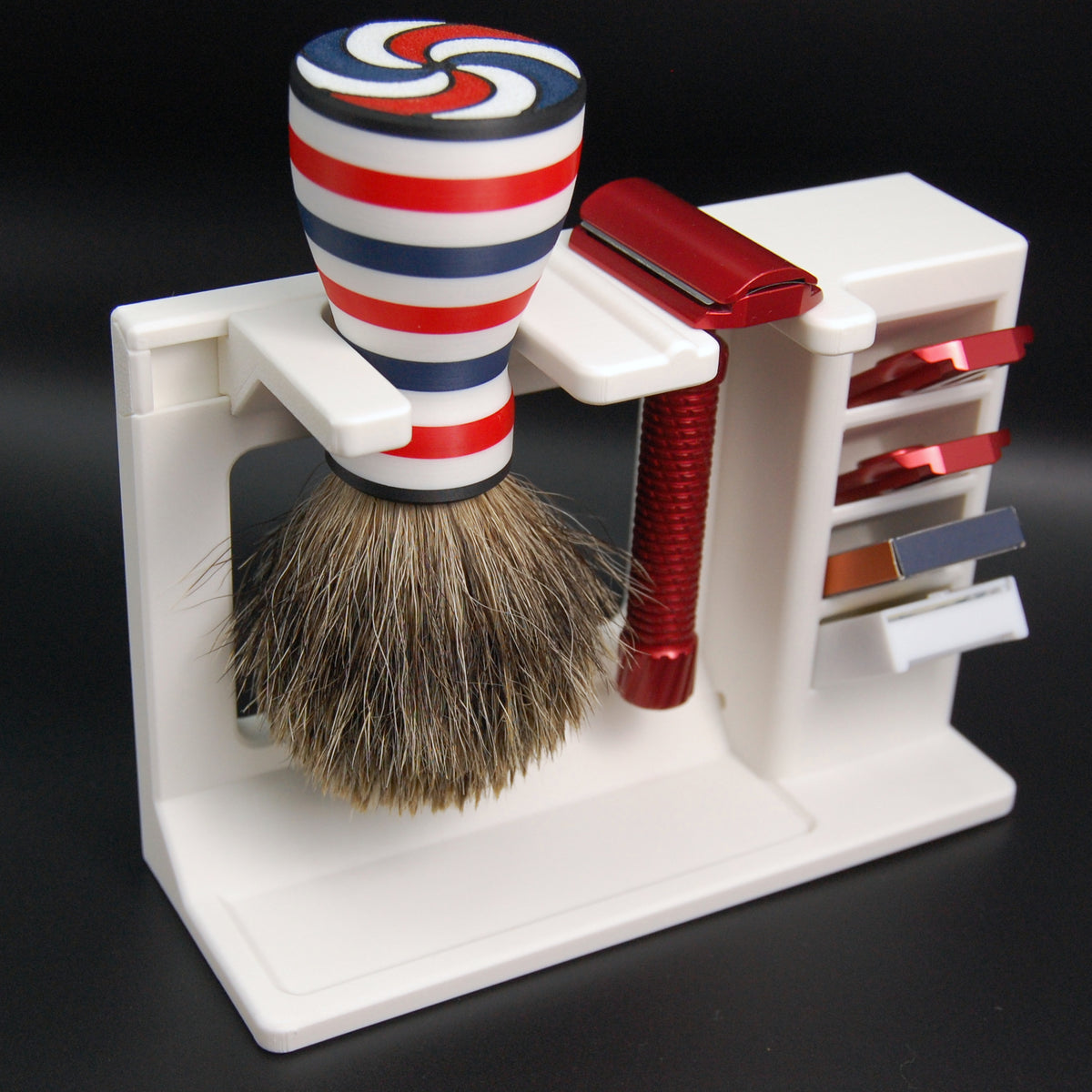 Red adjustable safety razor with four base plates and red-white-blue striped shaving brush displayed on a white stand