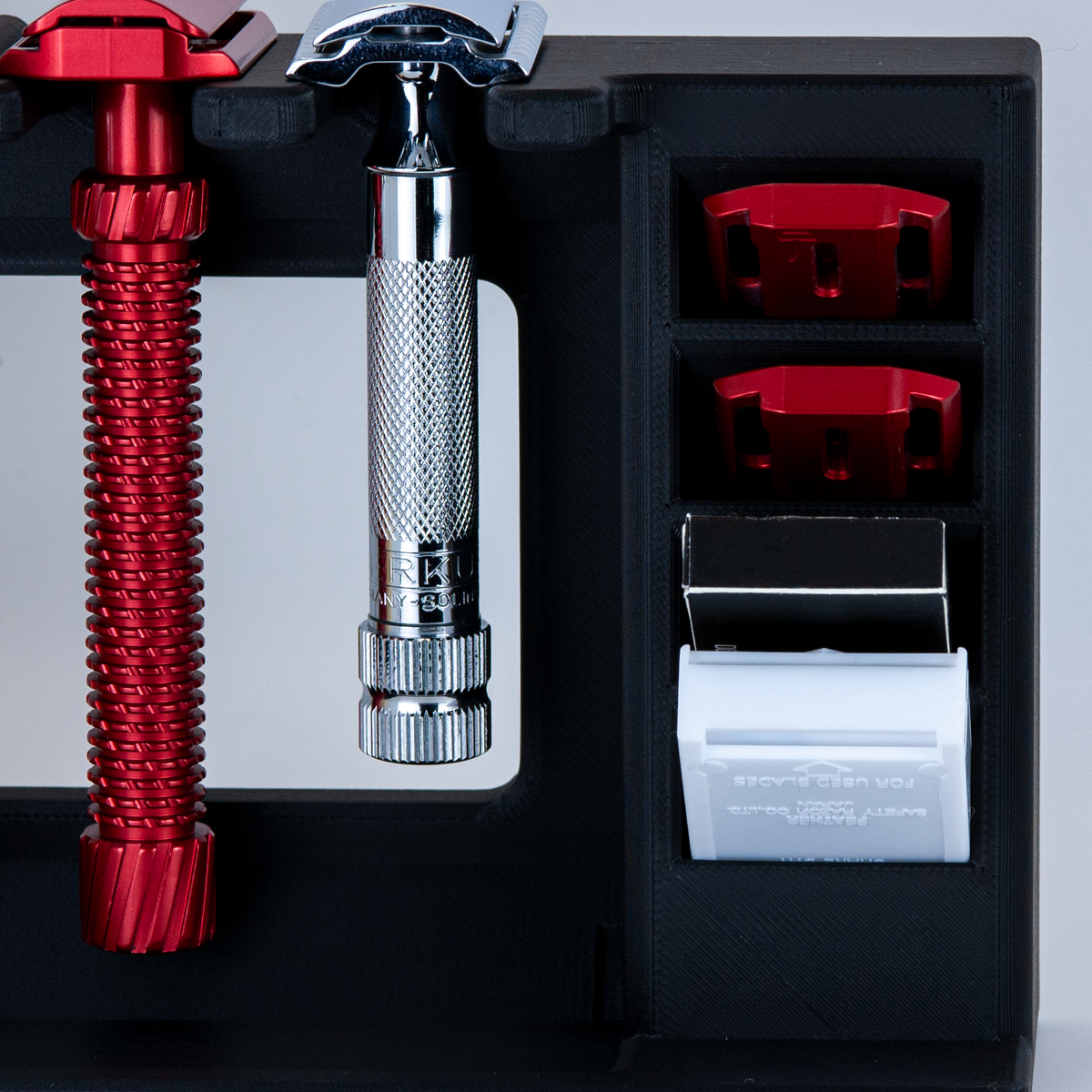 Black Mission Control two-razor countertop shave organizer with a red Oliworks razor and chrome Merkur razor hanging in the stand