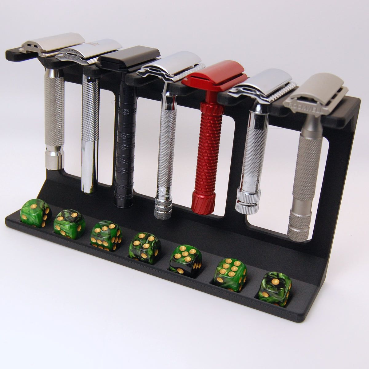 Black matte razor display stand holding 7 safety razors in various finishes with 7 green marbled dice in bottom slots