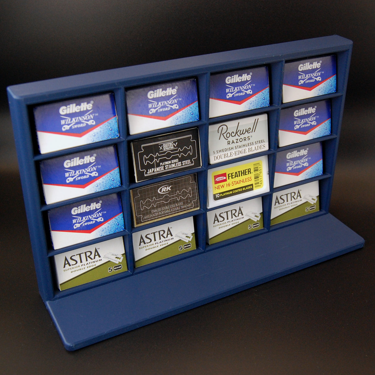 Navy blue razor blade display stand holding Astra, Gillette, Shaving Revolution, RK, Rockwell, and Feather blade tucks on a black background.
