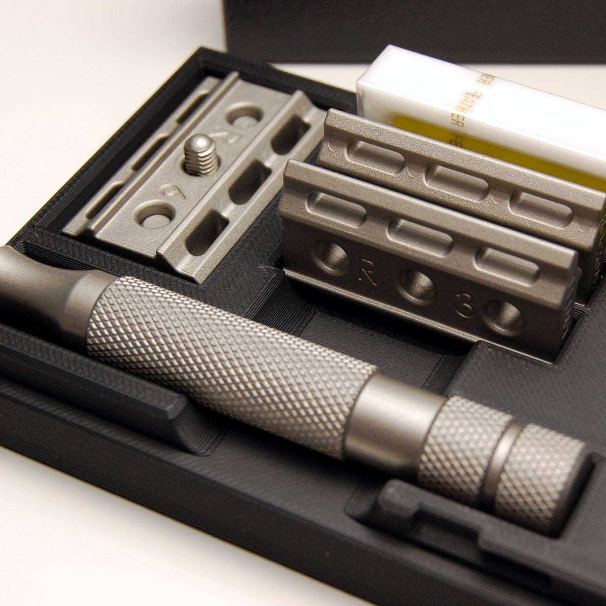 Rockwell travel case with deep slot holding a plate and blade on the head, handle and extra plates in fitted compartments, and a 10-pack of Feather razor blades.
