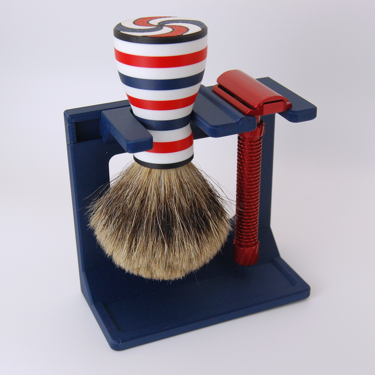 Shaving brush with red, white, and blue stripes in a stand with a red razor on a white background
