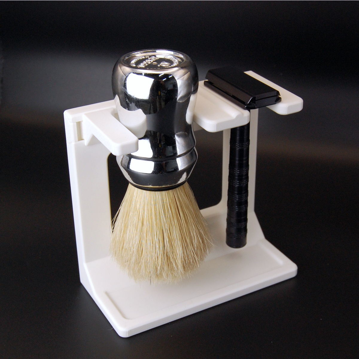 White shave staging stand with omega brush and black henson razor on a black background.