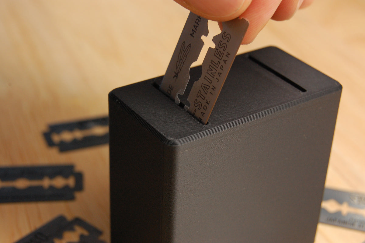 Feather razor blade being inserted into the Graveyard Orbit blade bank on a wooden surface with scattered razor blades.