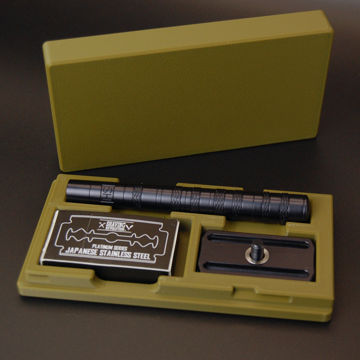 Army green Henson case on black background with black Henson razor inside and Shaving Revolution Japanese stainless steel blade tuck.