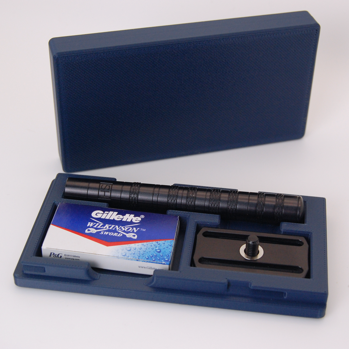 Navy blue Henson case on white background with black Henson razor stored inside and a Gillette Wilkinson Sword blade tuck.