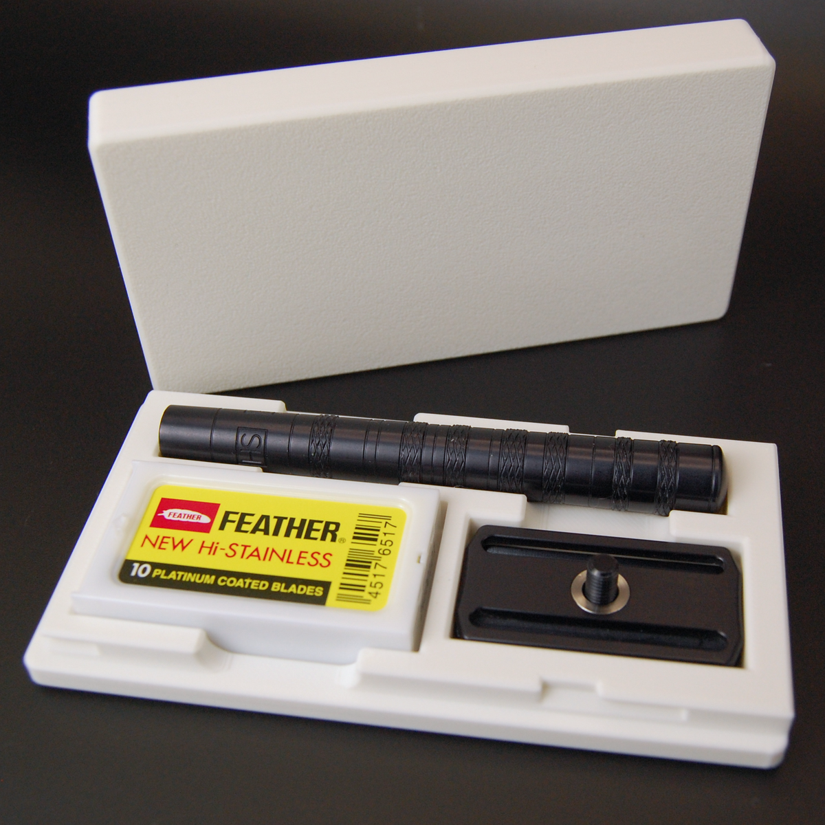Henson white case on black background with black Henson razor inside and Feather New Hi-Stainless razor blade tuck.