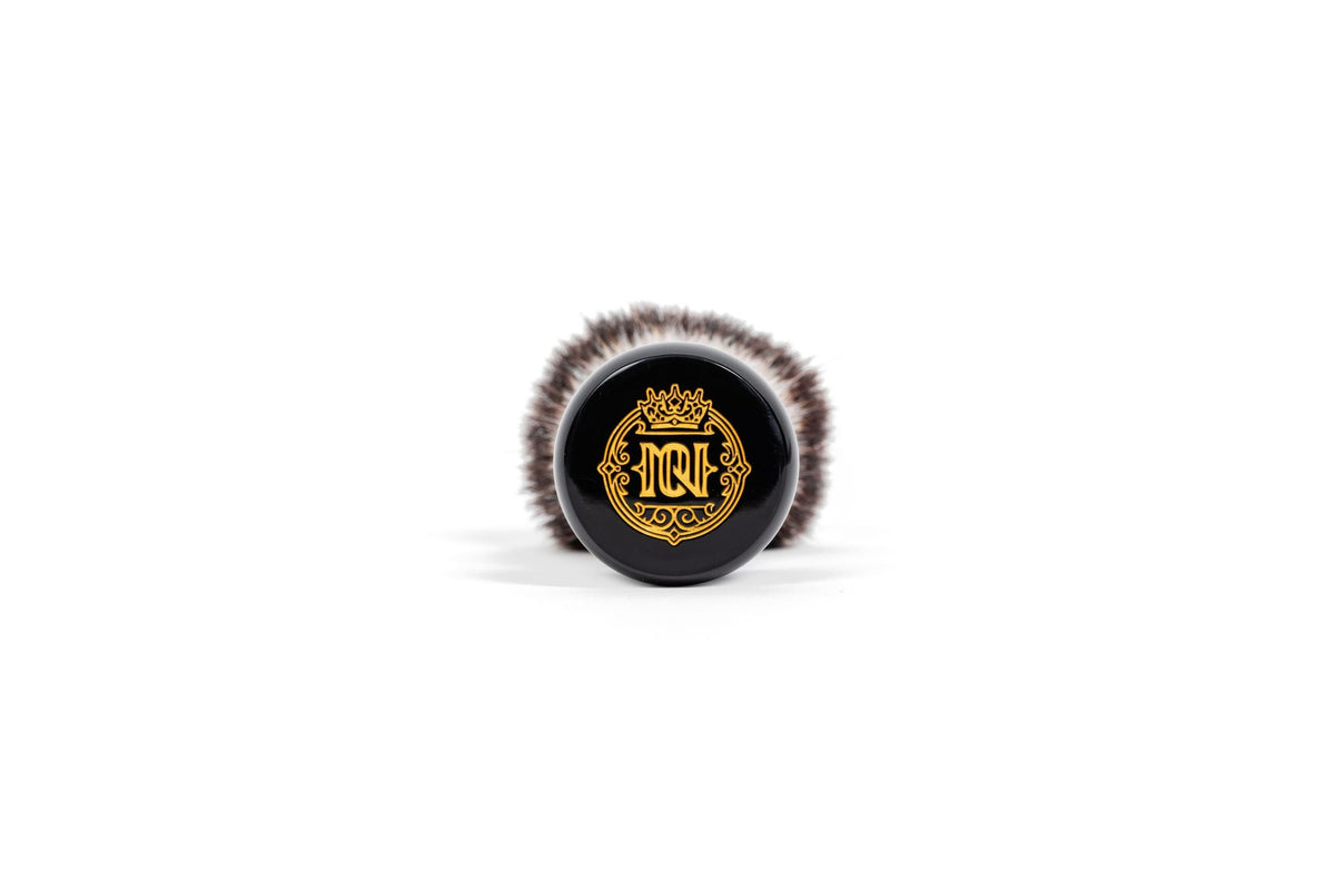 Bottom view of Noble Otter 26mm synthetic shave brush with black handle, gold MQF crown logo, and white-tipped bristles