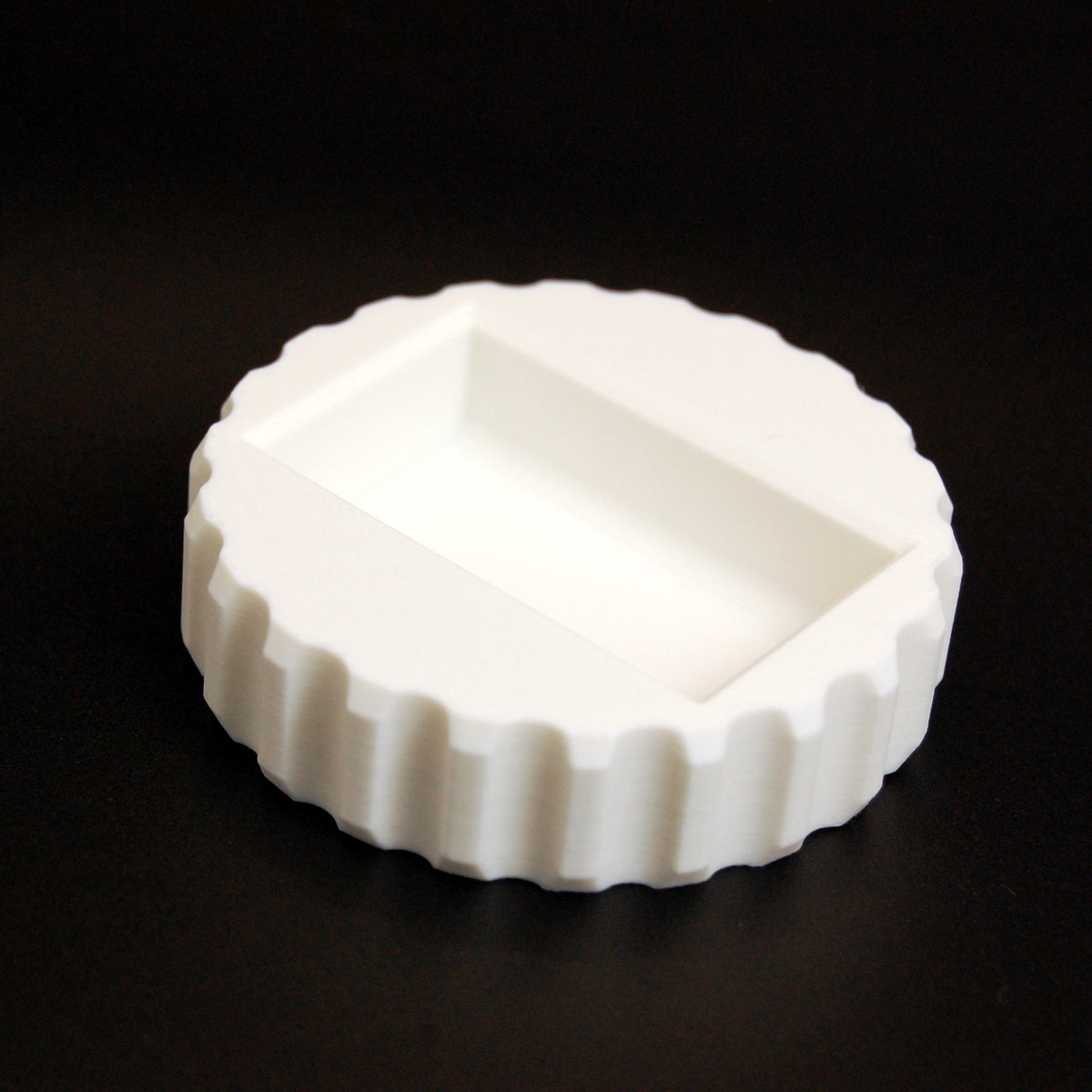 White round scalloped-edge 3D-printed razor blade change tool with rectangular recessed compartment on top