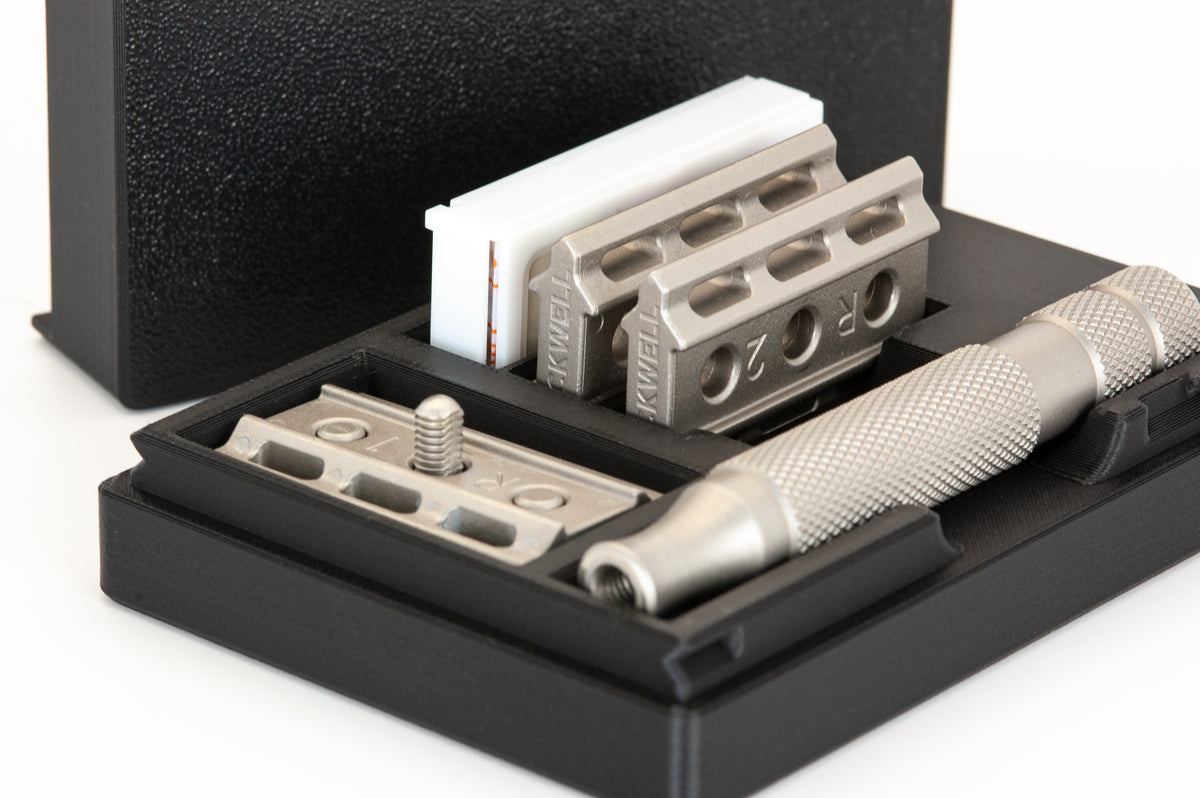 Angled close-up of the open black Rockwell 6S case: base plate with stud, R2 plates stacked, knurled handle, blade box behind