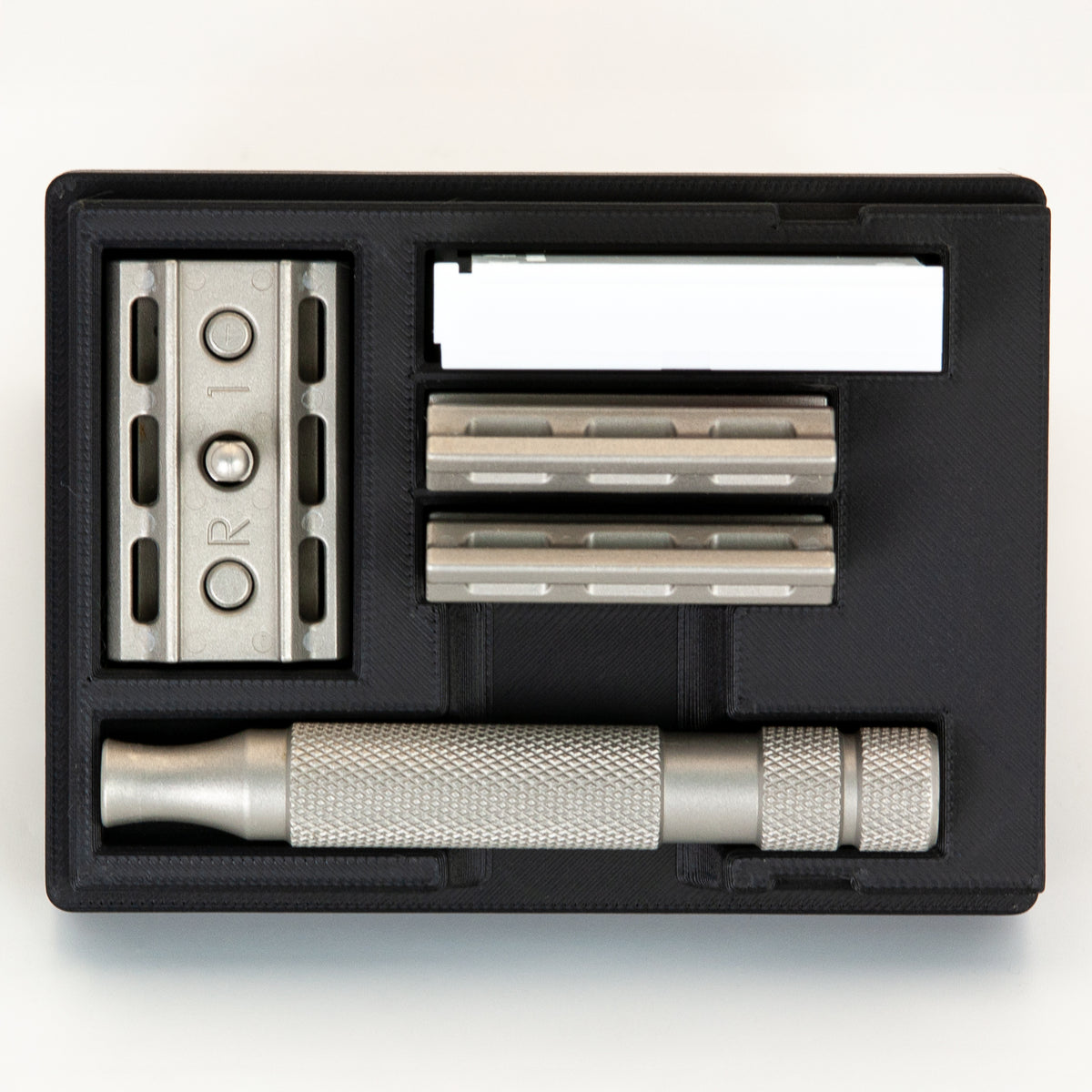 Black Rockwell 6S razor travel case open from above: stainless base plate, two plates, handle and blade box each in its bay