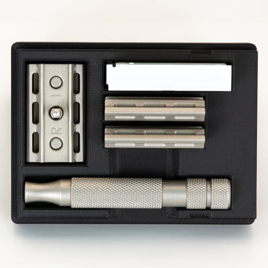 Black Rockwell 6S razor travel case open from above: stainless base plate, two plates, handle and blade box each in its bay