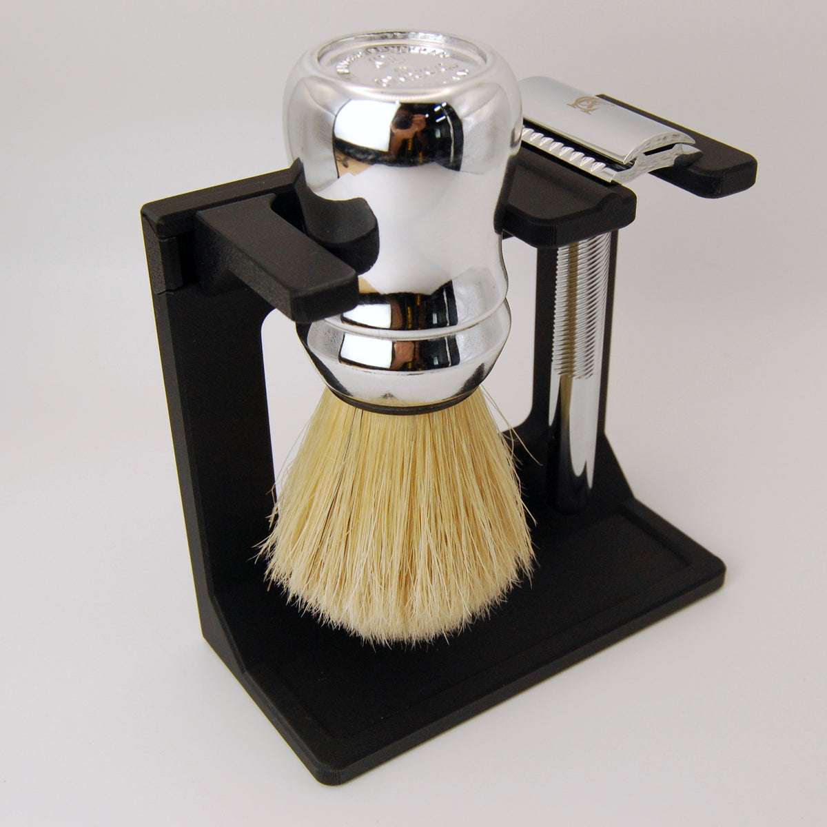 Shaving brush with black stand and chrome razor on a white background