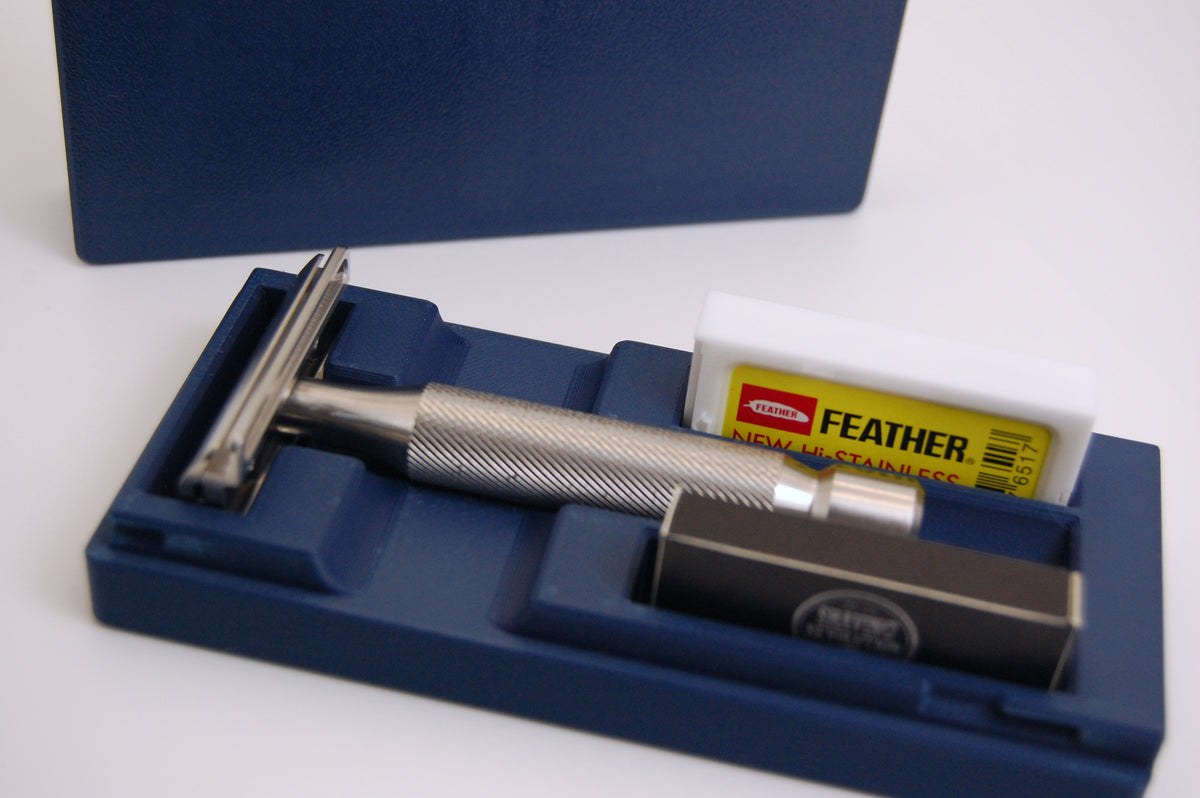 Blue hinged travel case holding a silver knurled double-edge safety razor and Feather New Hi-Stainless blade pack