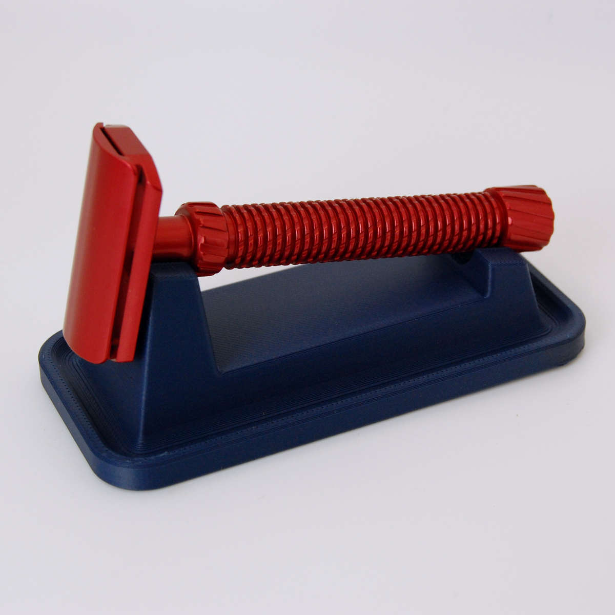 Universal razor stand with drip tray in navy blue on a white background.  Pictured with a red Oliworks M3teorite razor.