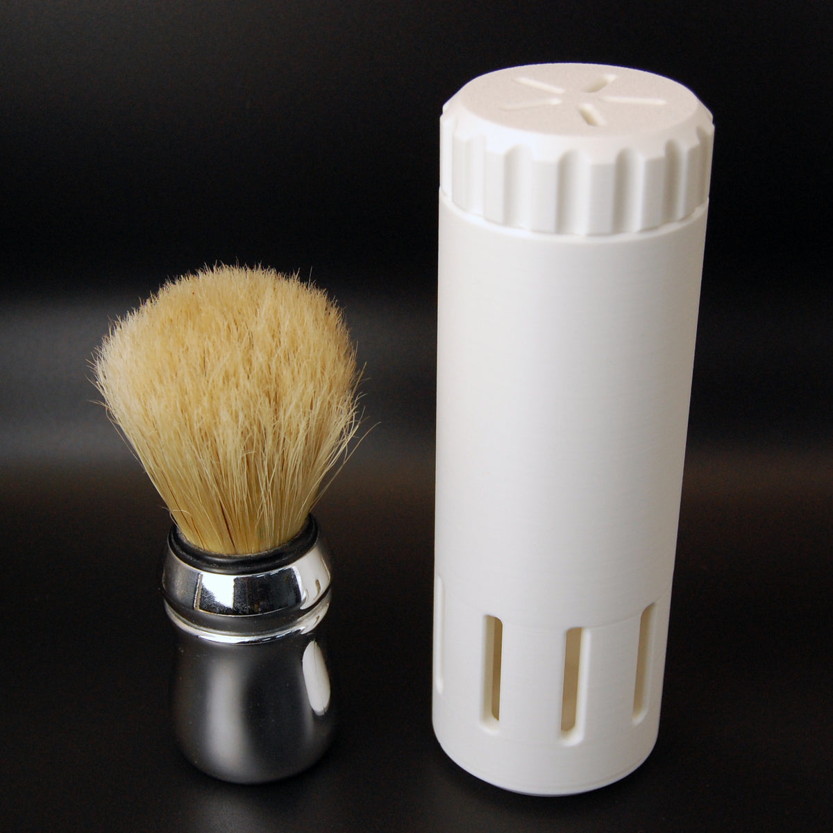 White vented shaving brush travel case on a black background with a brush sitting next to it.